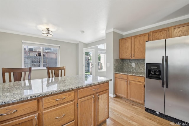 kitchen featuring light wood finished floors, ornamental molding, light stone countertops, decorative backsplash, and stainless steel fridge
