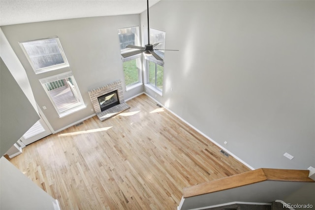 unfurnished living room with wood finished floors, visible vents, a ceiling fan, baseboards, and a brick fireplace