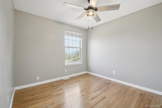 empty room with wood finished floors, visible vents, a ceiling fan, and baseboards