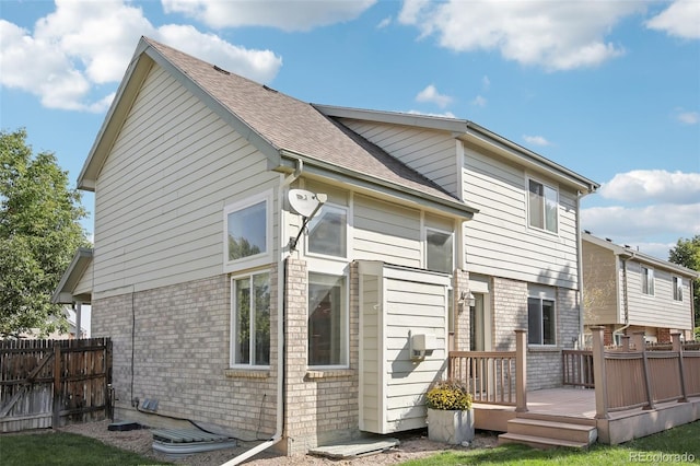 back of property featuring brick siding, roof with shingles, fence, and a deck