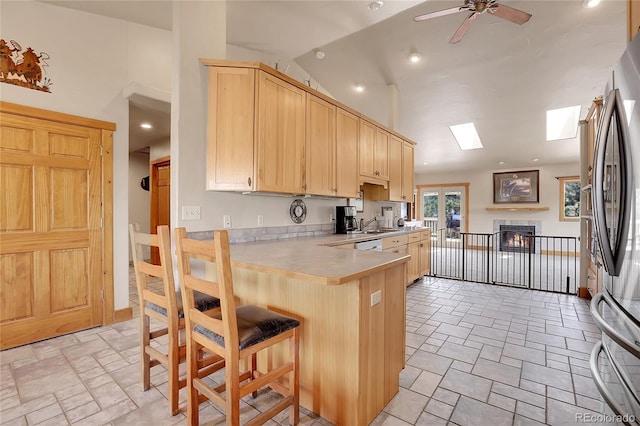 kitchen featuring stainless steel refrigerator, a skylight, a breakfast bar, light brown cabinets, and kitchen peninsula