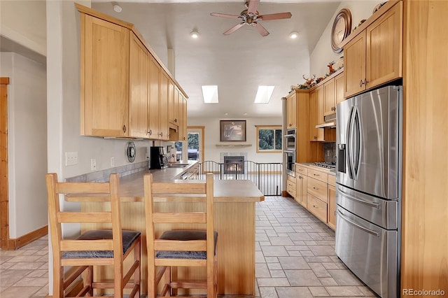 kitchen featuring light brown cabinets, a skylight, kitchen peninsula, appliances with stainless steel finishes, and a kitchen bar