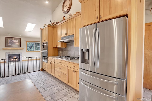 kitchen with stainless steel appliances, light brown cabinetry, backsplash, and a skylight