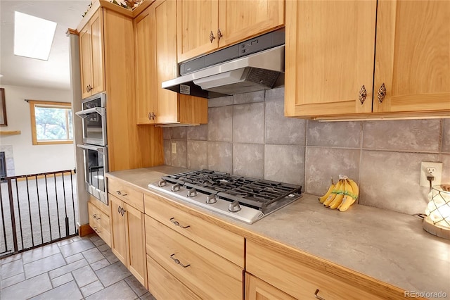 kitchen with light brown cabinetry, a skylight, appliances with stainless steel finishes, and tasteful backsplash