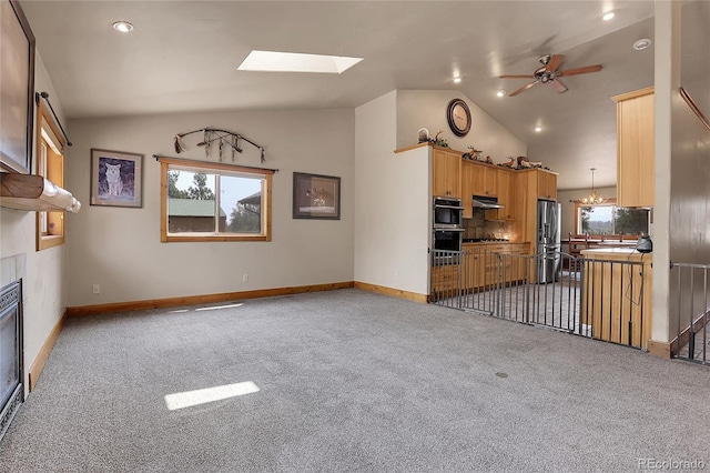 unfurnished living room with ceiling fan with notable chandelier, a skylight, carpet flooring, and high vaulted ceiling