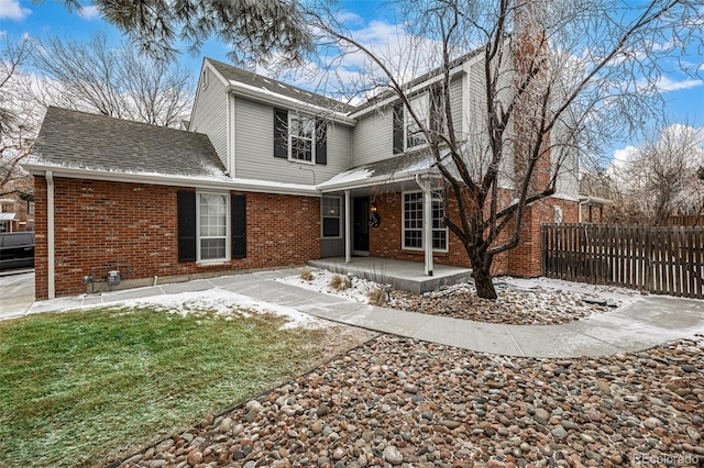 rear view of property with a shingled roof, fence, a lawn, and brick siding