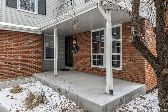 snow covered property entrance with brick siding