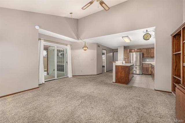 kitchen featuring a center island with sink, light colored carpet, freestanding refrigerator, brown cabinetry, and a sink