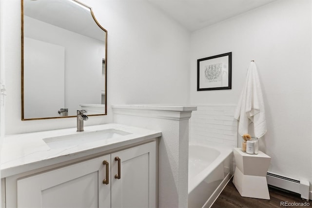 bathroom featuring a baseboard heating unit, hardwood / wood-style floors, a washtub, and vanity