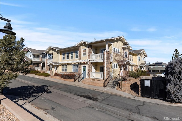 view of front of house featuring a balcony, stone siding, a residential view, and fence