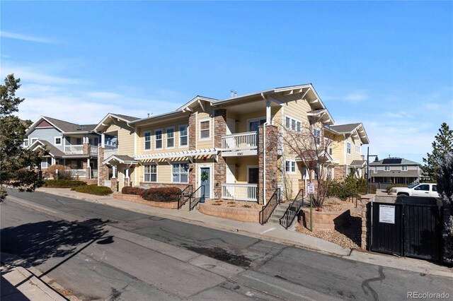 view of front facade featuring a balcony, stone siding, a residential view, and fence