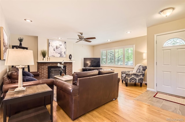 living area featuring a ceiling fan, light wood finished floors, a brick fireplace, recessed lighting, and baseboards