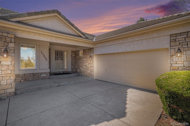 13806 E Chenango Dr, Aurora, CO 80015 - exterior entry at dusk with stone siding, driveway, a garage, a tile roof, and stucco siding