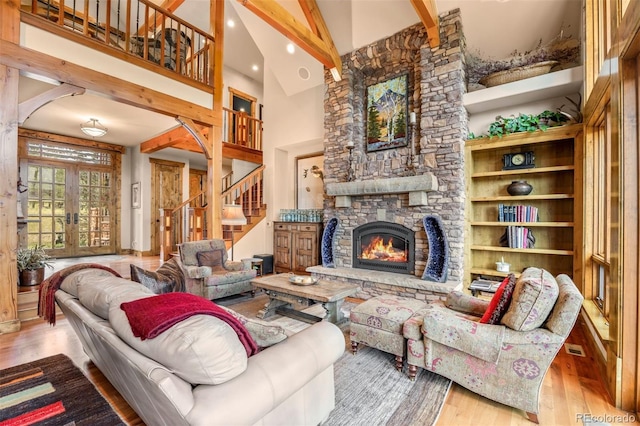 living room featuring french doors, light hardwood / wood-style floors, high vaulted ceiling, a fireplace, and beamed ceiling