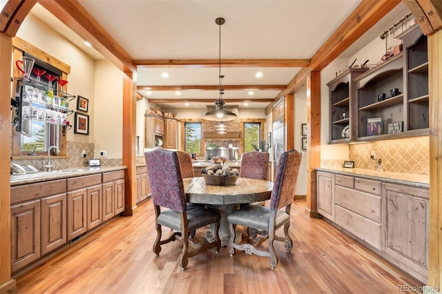 dining space with sink, light wood-type flooring, and beamed ceiling