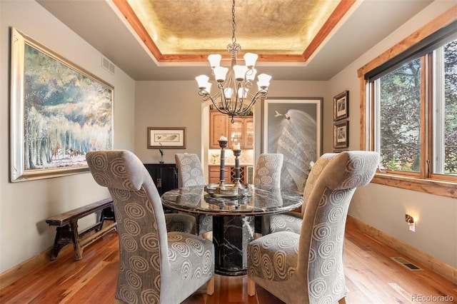 dining area with a notable chandelier, light hardwood / wood-style floors, and a raised ceiling