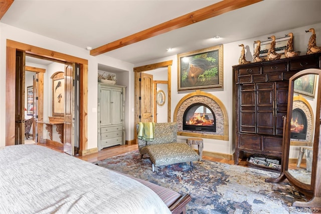 bedroom featuring a multi sided fireplace, light hardwood / wood-style flooring, and beamed ceiling