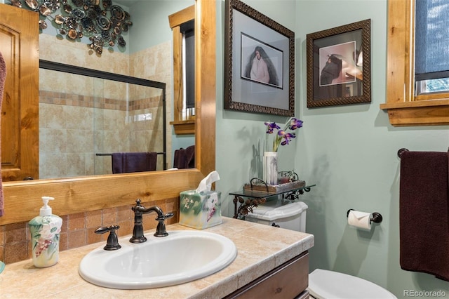 bathroom featuring toilet, vanity, decorative backsplash, and a shower with shower door