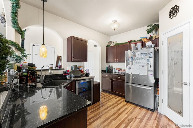 kitchen featuring sink, wine cooler, dark stone countertops, stainless steel fridge, and decorative light fixtures