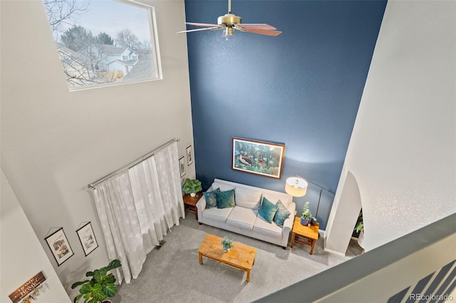 carpeted living room with ceiling fan and a high ceiling