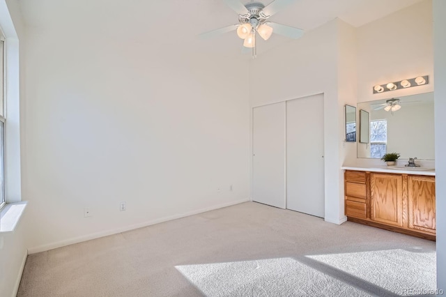 unfurnished bedroom featuring ceiling fan, a closet, light carpet, and sink