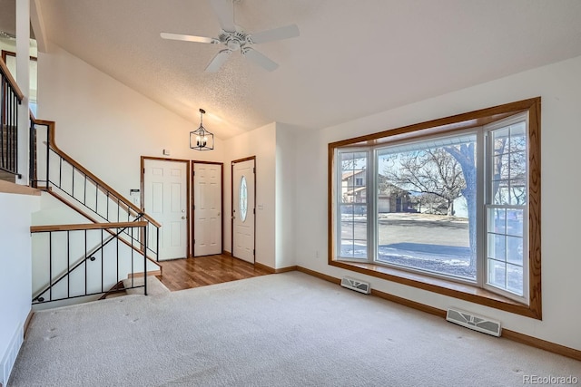 entryway featuring ceiling fan with notable chandelier, a textured ceiling, light carpet, and vaulted ceiling