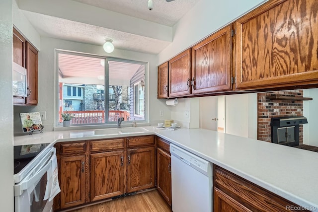 kitchen with sink, a textured ceiling, white appliances, light hardwood / wood-style floors, and kitchen peninsula