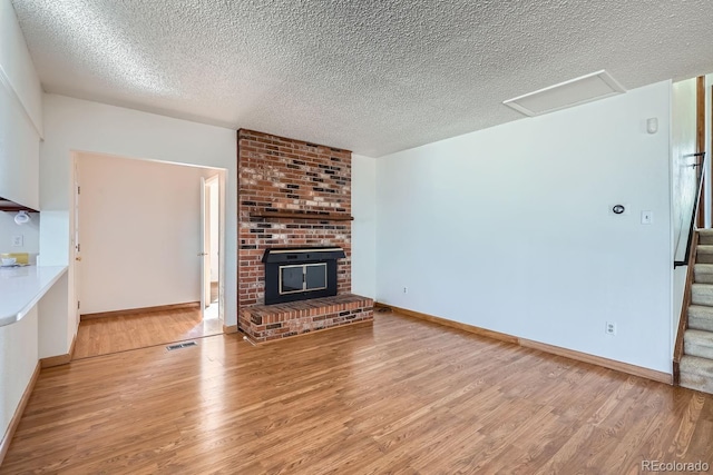 unfurnished living room featuring a brick fireplace, a textured ceiling, and light wood-type flooring