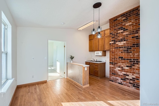 kitchen featuring sink, a textured ceiling, light hardwood / wood-style flooring, and hanging light fixtures