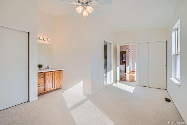 bedroom with ceiling fan, light colored carpet, connected bathroom, and vaulted ceiling