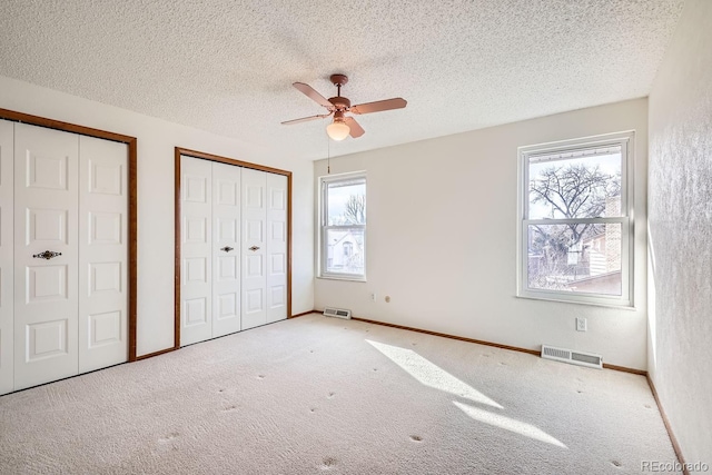 unfurnished bedroom featuring multiple closets, ceiling fan, multiple windows, and carpet flooring