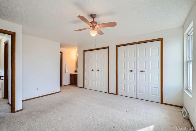 unfurnished bedroom with connected bathroom, multiple closets, ceiling fan, and light colored carpet