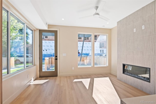 unfurnished living room with ceiling fan, tile walls, a tile fireplace, baseboards, and light wood finished floors
