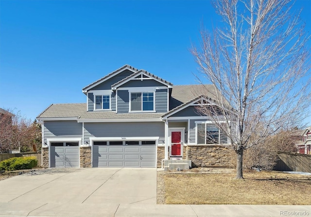 craftsman-style home featuring stone siding, fence, a tiled roof, and concrete driveway