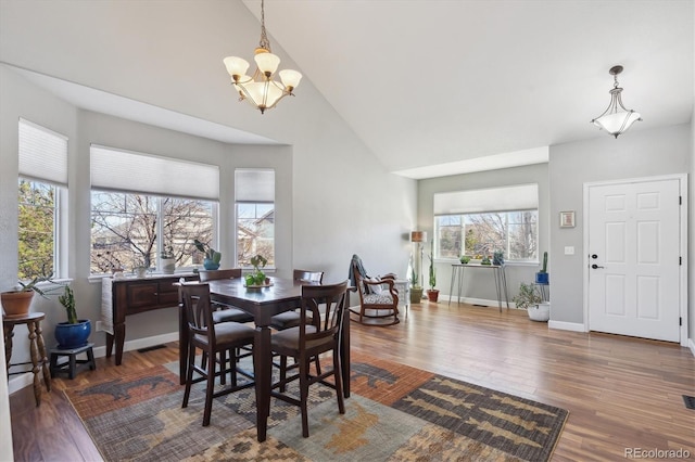 dining room with high vaulted ceiling, a notable chandelier, baseboards, and wood finished floors