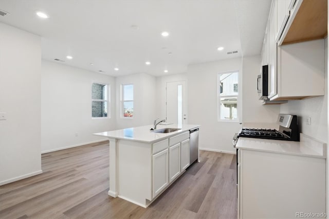 kitchen with a kitchen island with sink, sink, light hardwood / wood-style flooring, appliances with stainless steel finishes, and white cabinetry