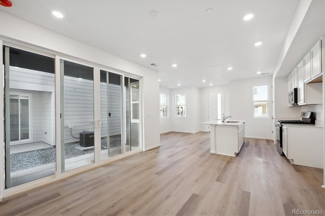 kitchen featuring white cabinetry, sink, a kitchen island with sink, appliances with stainless steel finishes, and light wood-type flooring