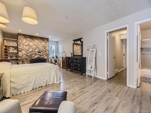 bedroom featuring a fireplace, a textured ceiling, ensuite bath, and light wood-type flooring