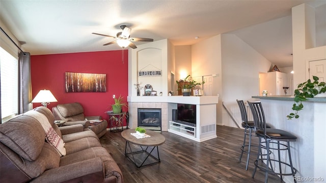 living room with dark wood finished floors, lofted ceiling, ceiling fan, and a tiled fireplace