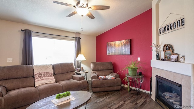 living area featuring vaulted ceiling, dark wood-style floors, a ceiling fan, a tile fireplace, and baseboards