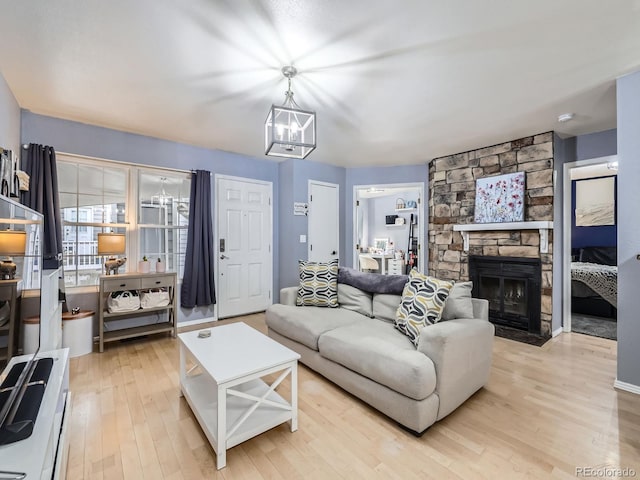 living room with a stone fireplace, light hardwood / wood-style flooring, and an inviting chandelier