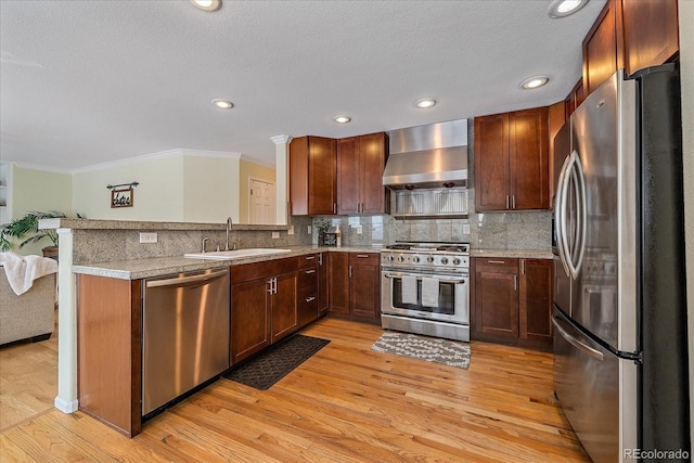 kitchen with sink, stainless steel appliances, kitchen peninsula, wall chimney exhaust hood, and light wood-type flooring