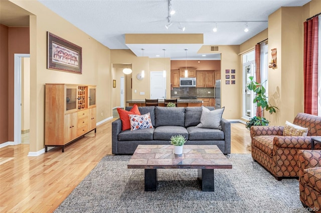 living area with light wood-type flooring, baseboards, visible vents, and a textured ceiling