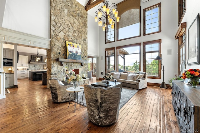 living area with high vaulted ceiling, hardwood / wood-style floors, a chandelier, a stone fireplace, and baseboards
