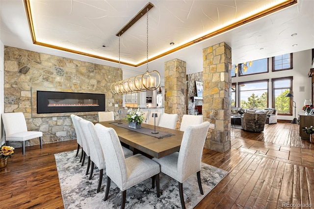 dining area featuring a raised ceiling, hardwood / wood-style flooring, a fireplace, ornate columns, and a chandelier