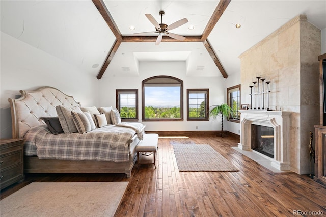 bedroom featuring wood-type flooring, a tiled fireplace, beam ceiling, high vaulted ceiling, and baseboards