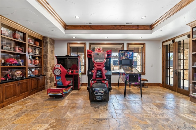 game room featuring french doors, a raised ceiling, baseboards, stone tile floors, and crown molding