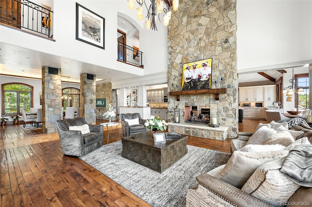 living area with a towering ceiling, dark wood-style floors, a chandelier, decorative columns, and a fireplace