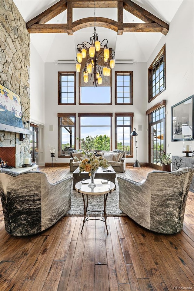 living room with high vaulted ceiling, hardwood / wood-style flooring, a chandelier, beam ceiling, and a stone fireplace