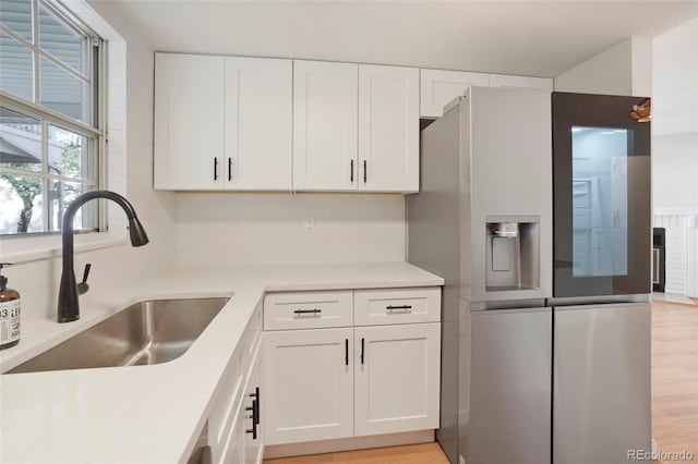 kitchen with stainless steel fridge, backsplash, light wood-type flooring, sink, and white cabinets